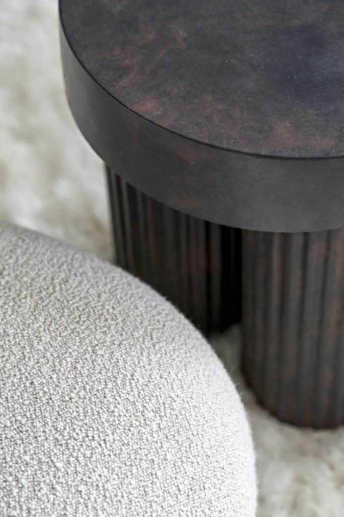 Luxurious drawing room showcasing an up close textures with a fluffy rug, boucle fabric armchair, and a dark stone three-legged side table.