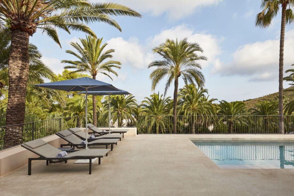 Pairs of modern sun loungers beside a pool in natural stone.