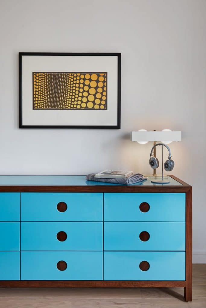 A bright blue lacquered chest of drawers adds a pop of colour to this bedroom.