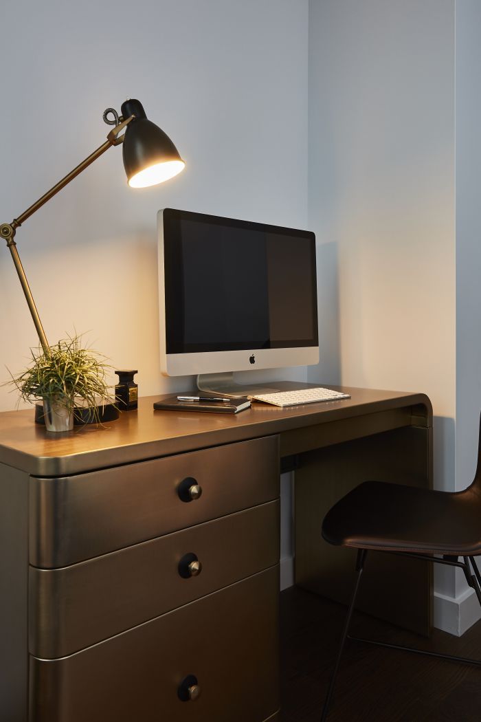 A modern brass desk creates a study area in the corner of a bedroom. 