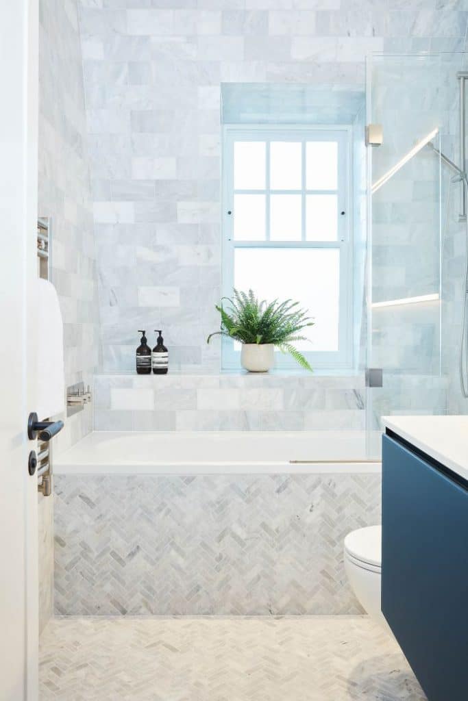 Subway carrara marble family bathroom with Turkish Carrara herringbone tiled floor.