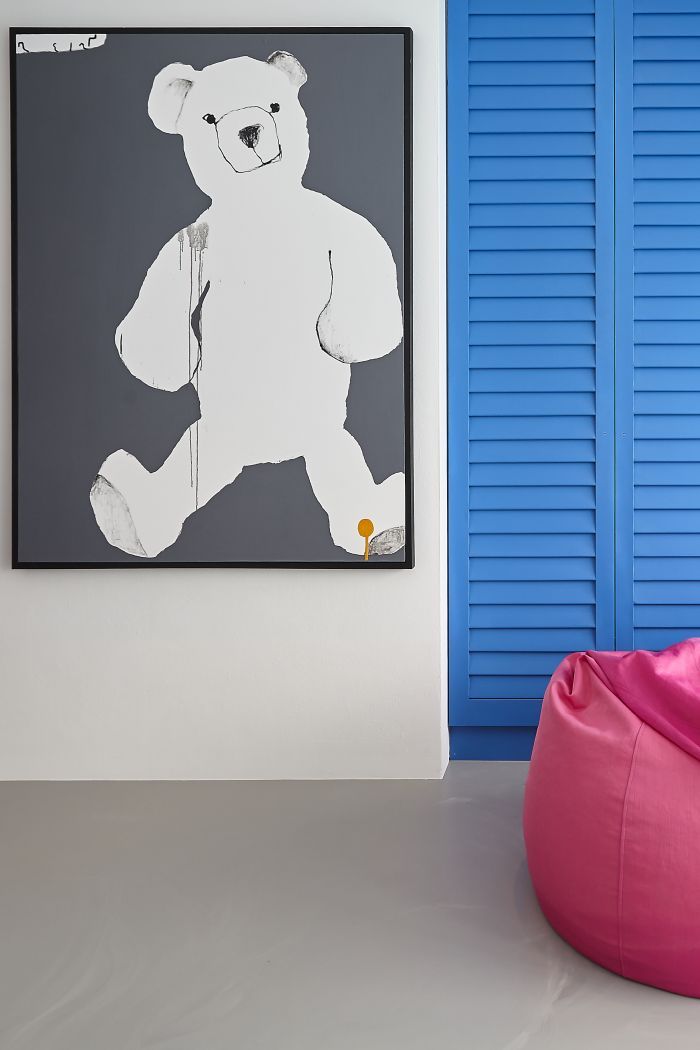 A large oil painting of a teddy in a kids bedroom with blue wardrobes and resin flooring. 