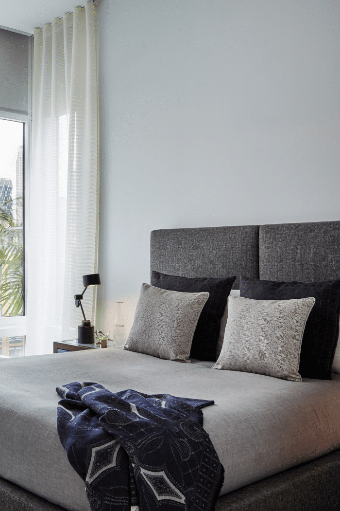 Crisp white bedroom furnished with blue and grey fabric headboard, throws and pillows. 