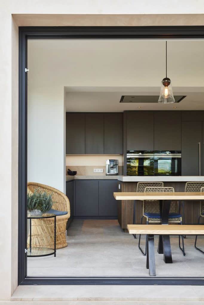 Rattan armchairs sit in the corner of an open plan kitchen and dining room in contemporary Majorca villa.