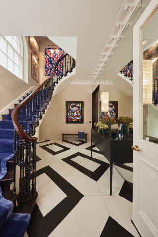 An image of a black and white marble floor entrance in London period property. From the entrance a large staircase with navy blue carpet leads up to the next floor.