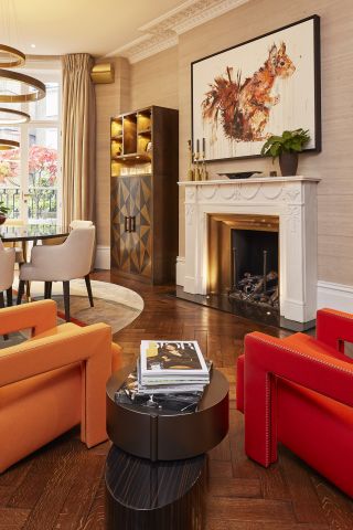 Two bright coloured modern armchairs around a marble fireplace.