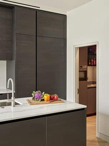 Kitchen with dark cabinetry and neutral walls in center and door opening to pantry in the back.