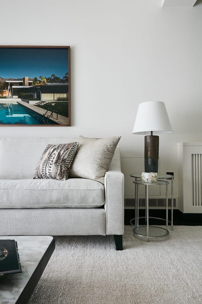 Neutral living space with colourful artwork above sofa and glass side table.