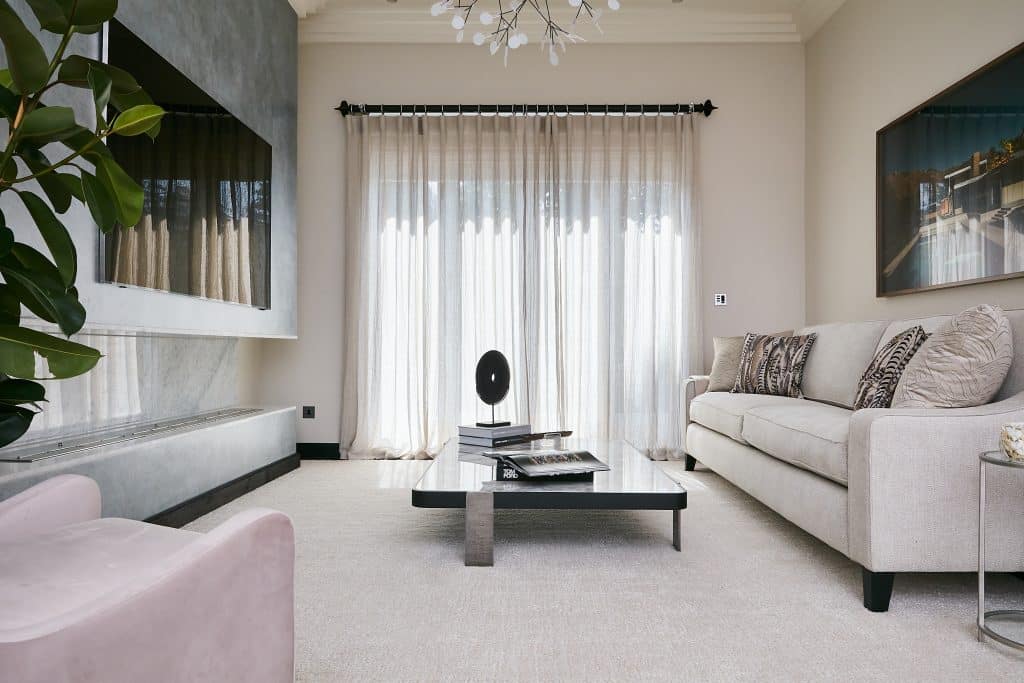 Neutral media room with blush pink armchair and marble top coffee table.