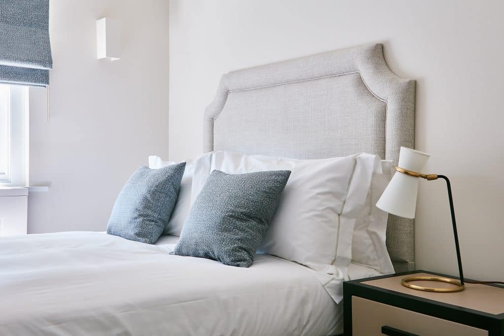 Neutral bed with grey cushions which match the colour of the window blinds.