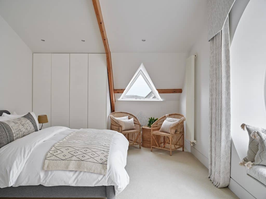 Mezzanine bedroom with glass walls looking down into the living area are concealed with lush, floor skimming drapes from which instantly add warmth. Built-in wardrobes make maintaining a clean and tidy space easy, and a playful assortment of bedding materials add tactile decor.