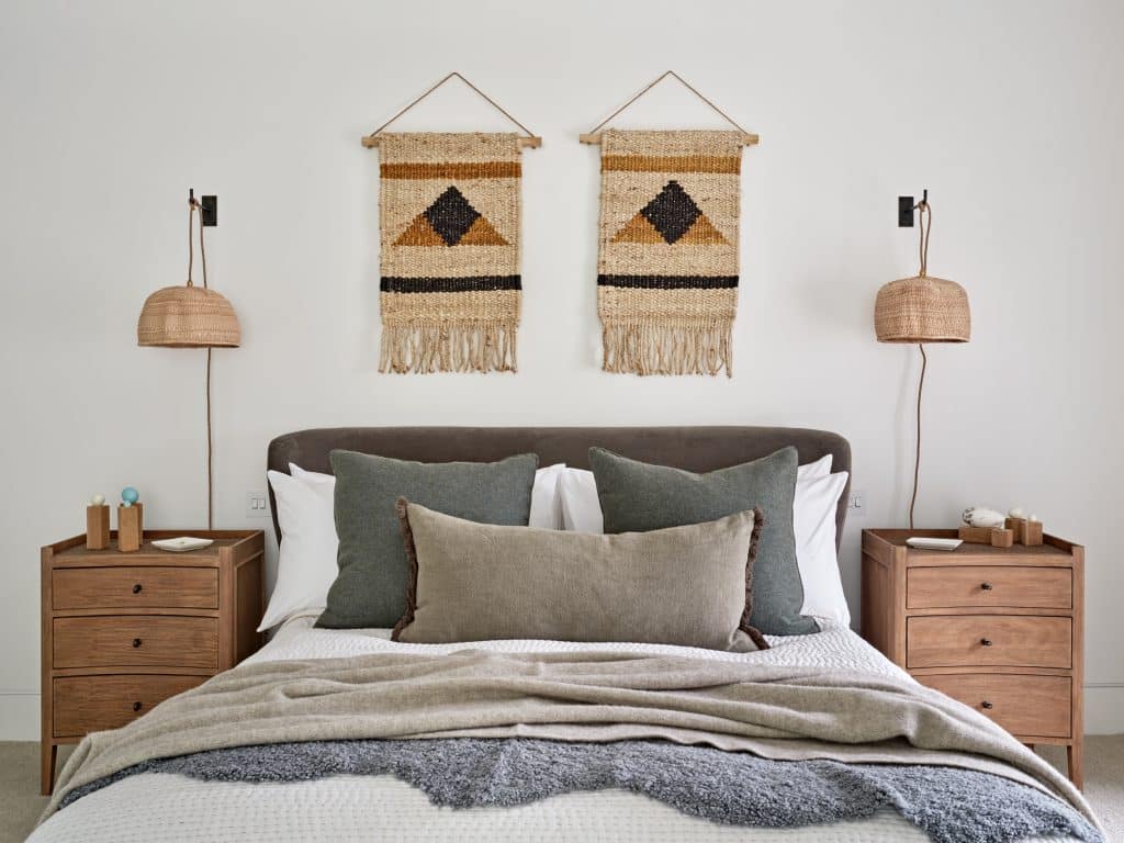 Neutral bedroom in coastal style house. The bedroom is decorated with rattan lampshades and brown bedside tables.